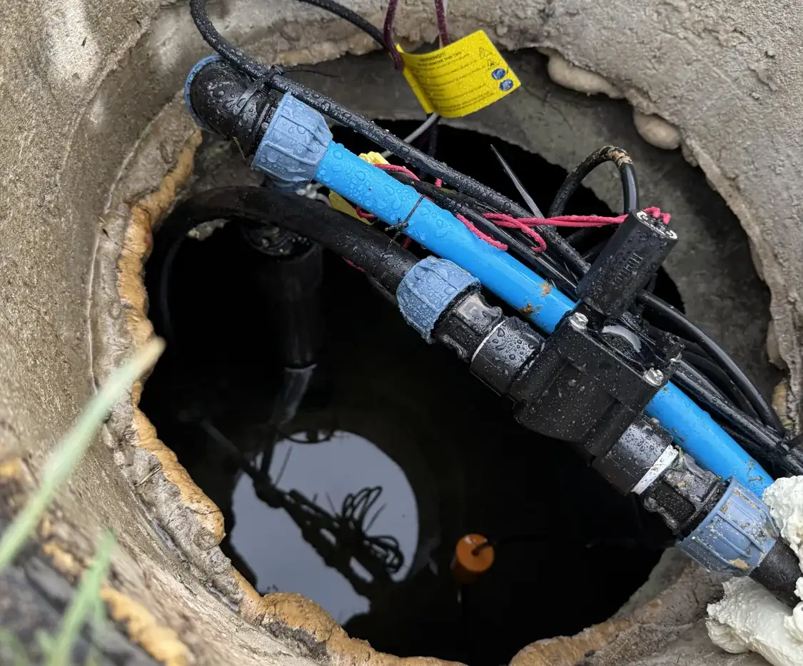 Widok z góry do betonowego zbiornika z wodą: rura od pompy, elektrozawór, przewody zasilające i sterujące oraz pływak